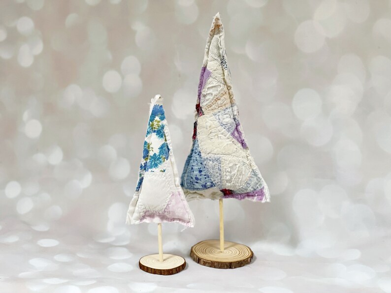 May include: Two fabric Christmas trees on wooden bases. The larger tree is made of white fabric with purple, blue, and pink floral patterns. The smaller tree is made of white fabric with blue floral patterns.