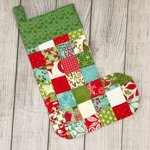 May include: A red and green patchwork Christmas stocking with a white cuff. The stocking is made of various fabrics with different patterns, including floral, geometric, and plaid.