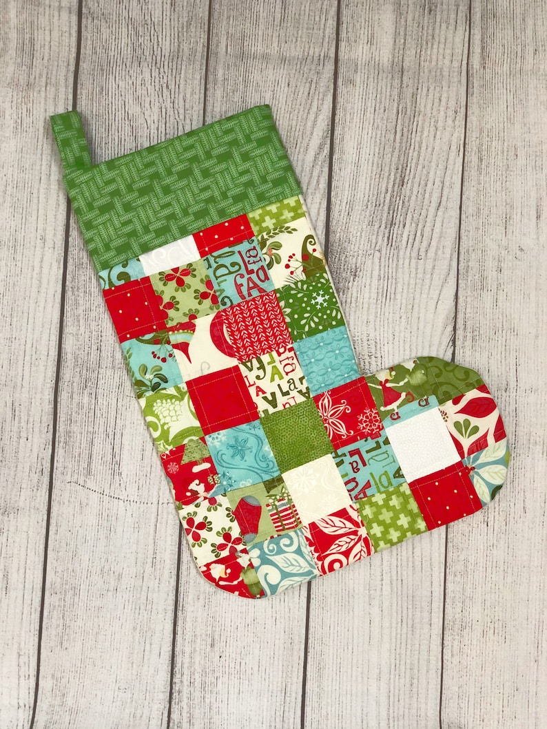 May include: A red and green patchwork Christmas stocking with a white cuff. The stocking is made of various fabrics with different patterns, including floral, geometric, and plaid.
