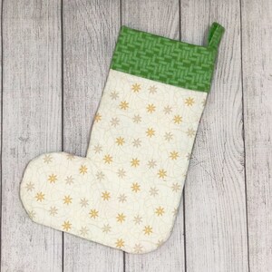 May include: A white Christmas stocking with a green and white patterned cuff. The stocking is decorated with a gold star pattern.