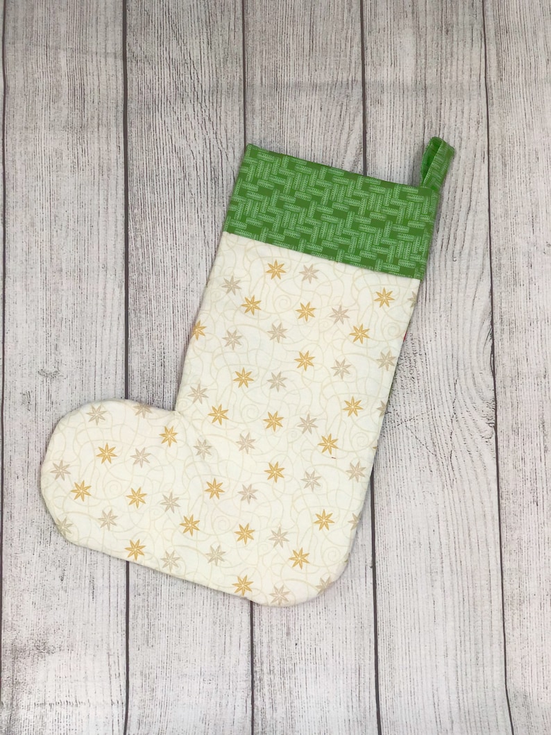 May include: A white Christmas stocking with a green and white patterned cuff. The stocking is decorated with a gold star pattern.