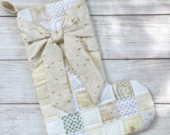 May include: A white and cream patchwork Christmas stocking with a gold bow and gold star accents.