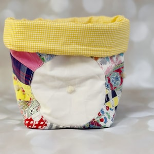 May include: A yellow gingham fabric-lined storage basket with a patchwork design featuring various floral and geometric patterns in pink, blue, red, and yellow.