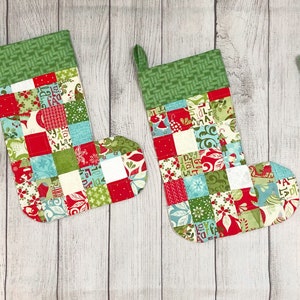 May include: Four patchwork Christmas stockings in red, green, white, and blue with a green and white checkered cuff.