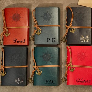 May include: Six leather-bound journals with compass designs and personalized names. The journals are brown, black, green, and red. Each journal has a leather strap and a metal anchor charm.