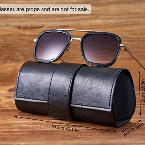 May include: Black leather sunglasses case with a strap closure. The case is 6.49 inches long, 2.36 inches wide, and 2.95 inches high. Sunglasses are not for sale.