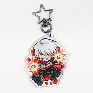 May include: A clear acrylic keychain featuring a cartoon character with white hair, blue eyes, and a red outfit, holding two guns. The keychain has a star-shaped clasp and a silver-colored metal ring.