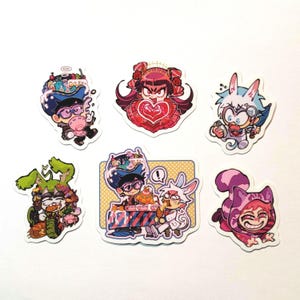 May include: A collection of six colorful stickers featuring cartoon characters with unique designs. The stickers showcase characters with bunny ears, heart-shaped motifs, and other whimsical elements. The stickers are on a white background.