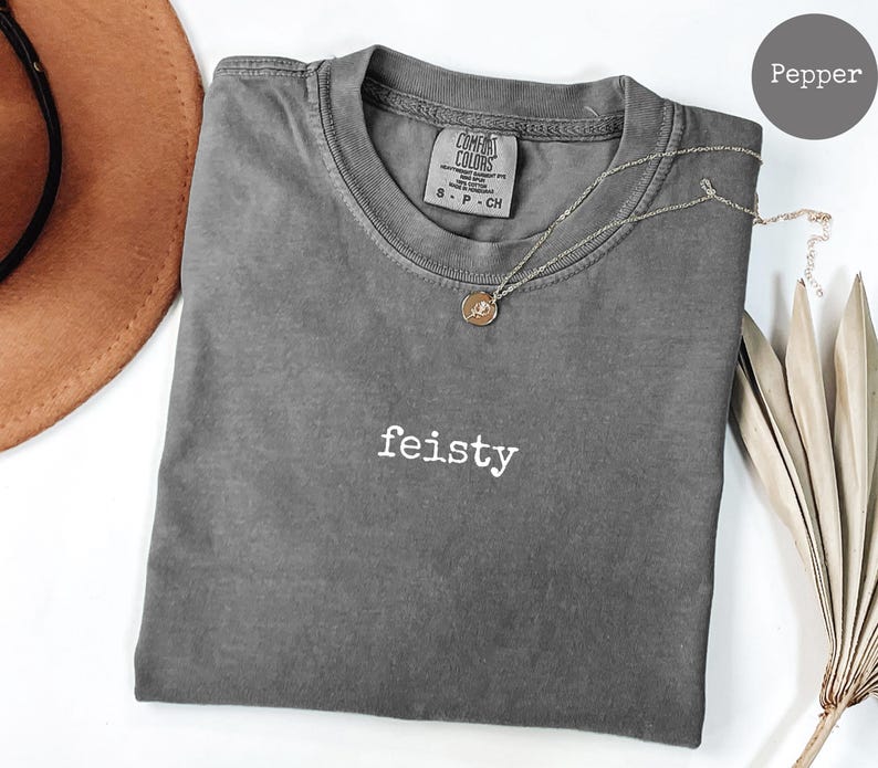 May include: A gray t-shirt with the word "feisty" printed in white on the front. The shirt is made of a soft, comfortable material and has a relaxed fit.