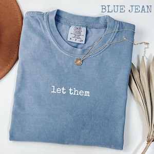May include: A blue jean t-shirt with the text "let them" printed in white on the front. The shirt is made of a soft, comfortable material and has a relaxed fit.