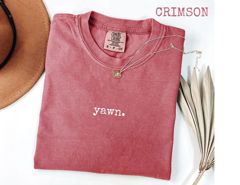 Peut inclure: T-shirt couleur cramoisi avec le mot "yawn." brod&eacute; en blanc. Un collier dor&eacute; avec un pendentif repose sur le t-shirt. Le t-shirt est de la marque Comfort Colors. Un chapeau marron et une plante s&eacute;ch&eacute;e sont en arri&egrave;re-plan.
