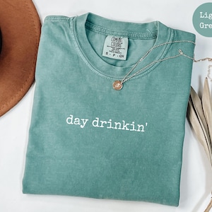 May include: Light green t-shirt with the text "day drinkin'" in white. The shirt is made of a soft, comfortable fabric.