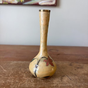 May include: A small, vintage vase with a cream-colored body and a gold rim. The vase features a hand-painted floral design with red and green accents. The vase is approximately 6 inches tall.