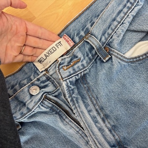 May include: Light blue denim jeans with a relaxed fit. The jeans feature a zipper fly, a button closure, and belt loops. The tag reads "RELAXED FIT".
