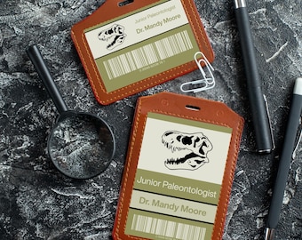 May include: Two brown leather ID badge holders with a dinosaur skull graphic and the text "Junior Paleontologist Dr. Mandy Moore".
