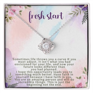 May include: A silver-toned necklace with a sparkling pendant, presented in a decorative box. The box features floral accents and the words "fresh start" in purple. The box also includes an inspirational message.