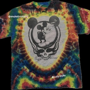 Puede incluir: Una camiseta teñida con un diseño en blanco y negro de Mickey Mouse fumando un cigarrillo, superpuesto a una calavera. La camiseta tiene un patrón en espiral en tonos de azul, amarillo, rojo y verde.