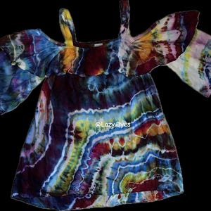 May include: A tie-dye dress with cold shoulder sleeves. The dress features a vibrant mix of colors, including blue, purple, yellow, and red. The text "@Lazy_Dyes" is visible on the lower part of the dress.