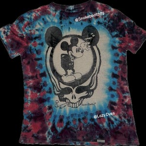Puede incluir: Camiseta teñida con un diseño de Mickey Mouse fumando un cigarrillo, superpuesto a un diseño de calavera. La camiseta está teñida en tonos de azul, rojo y morado, con el texto "This is a Bootleg" visible.