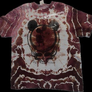 Puede incluir: Camiseta teñida con tinte anudado en burdeos y blanco con un gráfico de Mickey Mouse y una calavera de Grateful Dead. La camiseta presenta un patrón en espiral. Los textos "@snakebootzvtg" y "@Lazy Dyes" son visibles.