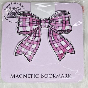 May include: A pink and white gingham bow-shaped magnetic bookmark with the text "MAGNETIC BOOKMARK" printed on the bottom.