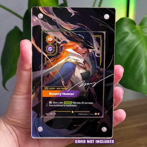 Può includere: Un espositore rettangolare in acrilico con un pannello frontale trasparente fissato da quattro viti argentate agli angoli. La custodia mostra una carta da gioco collezionabile intitolata Bounty Hunter con un personaggio dai capelli arancioni. Testo: CARD NOT INCLUDED.