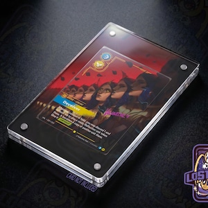 May include: A clear acrylic magnetic card display case holding a game card titled Deceiver. The card features an illustration of multiple figures with a red background, blue and yellow icons, and text. The case is secured with four silver corner screws.