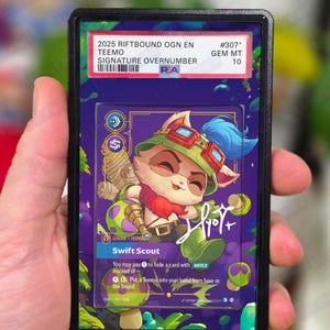 May include: A collectible card featuring a cartoon character, Teemo, in a protective case. The card has a signature and the text "2025 RIFTBOUND OGN EN TEEMO SIGNATURE OVERNUMBER". The card is graded GEM MT 10.
