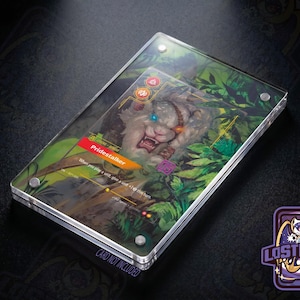 May include: A clear acrylic magnetic card display case holding a Pridestalker game card featuring a white creature with a blue eye in a jungle setting. The card displays text including Pridestalker and game mechanics. The case has four silver corner screws.