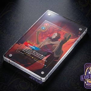May include: A rectangular clear acrylic display case with four silver corner screws, housing a collectible game card titled Virtuoso. The card features a character illustration in red and orange tones with game text and symbols. Card not included.