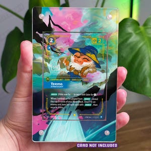 May include: A clear acrylic display case holding a Teemo Strategist card. The card features a cartoon character in a blue hat and outfit. The background is a mix of pink, blue, and green colours. The text "CARD NOT INCLUDED" is at the bottom.