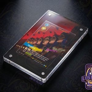 May include: A rectangular clear acrylic display case with four silver corner screws, housing a game card titled Deceiver. The card features an illustration of multiple figures with dark hair and red tones, with text detailing game mechanics.
