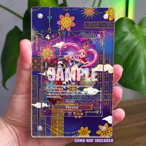 Op de afbeelding: Een rechthoekige acryl displayhouder met een paarse achtergrond en gouden en kleurrijke bloemmotieven. De houder bevat een One Piece verzamelkaart met het personage Perona met roze haar en een parasol, inclusief de tekst SAMPLE.