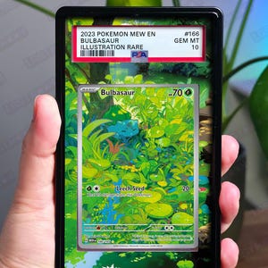 以下が含まれることがあります： 黒い長方形のPSA鑑定済みカードスラブ。2023年ポケモンMew EN Bulbasaur Illustration Rare #166 Gem Mt 10トレーディングカードが封入されている。カードには緑色のフシギダネのキャラクターが森の中に描かれており、Leech Seedというテキストが表示されている。