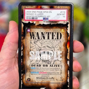 May include: A graded trading card featuring Monkey D. Luffy from One Piece. The card has a "Wanted" poster design with the text "DEAD OR ALIVE". The card is encased in a black holder with a red and white label.