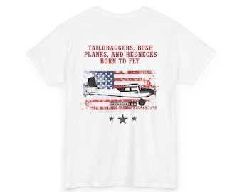 Puede incluir: Camiseta blanca con un diseño desgastado de la bandera estadounidense y un gráfico de avión. El texto dice: "TAILDRAGGERS, BUSH PLANES, AND REDNECKS BORN TO FLY." Debajo del gráfico hay tres estrellas. La camiseta es de cuello redondo.