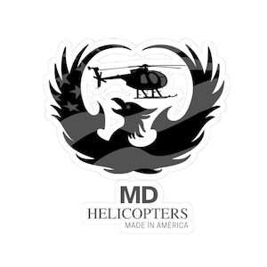 Könnte beinhalten: Ein Aufkleber mit einer schwarz-grauen Grafik eines Adlers mit ausgebreiteten Flügeln, die eine Hubschraubersilhouette und ein Flaggenmuster enthält. Unter der Grafik steht der Text MD HELICOPTERS MADE IN AMERICA in serifenloser Schrift.