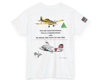 Puede incluir: Camiseta blanca con ilustraciones de aviones amarillos y rojos, con el texto "THE AIR TRACTOR ROARS, THE S-2 TANKER DIVES AND WE BRING THE FIGHT TO THE FIRE." Una pequeña bandera americana está en la manga derecha.