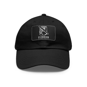May include: Black baseball cap with a curved brim. A white rectangular patch on the front displays the text "CIRRUS AIRCRAFT" below a graphic of an airplane propeller and wings.
