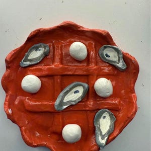 May include: A red, waffle-shaped sculpture with a grid pattern. It features white spheres and oyster-shaped elements with gray and white details. The artwork is a unique, food-themed piece.