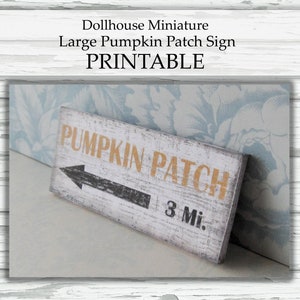 May include: A white wooden sign with black and gold lettering that reads "Pumpkin Patch 3 Mi.". The sign has a black arrow pointing to the left.