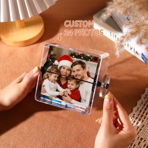 Puede incluir: Una pantalla de fotos giratoria transparente con una foto familiar en el interior. La pantalla tiene una ventosa en el lateral y el texto "CUSTOM 24 PHOTOS" encima. La foto muestra a una familia de cuatro miembros con ropa navideña.