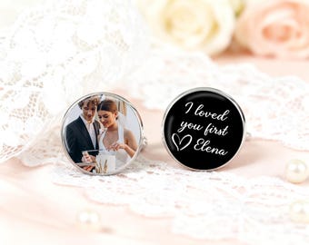 Op de afbeelding: Een paar zilveren manchetknopen. Eén manchetknop toont een foto van een stel, de andere heeft de tekst "I loved you first Elena" in wit op een zwarte achtergrond. De manchetknopen worden gepresenteerd op een roze ondergrond met kant en parels.