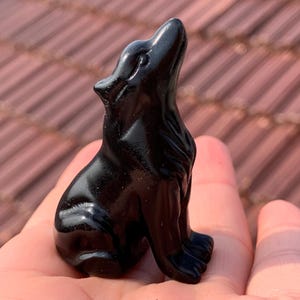 May include: Black obsidian wolf figurine carved in a sitting position with its head tilted up. The wolf has a shiny, polished finish.