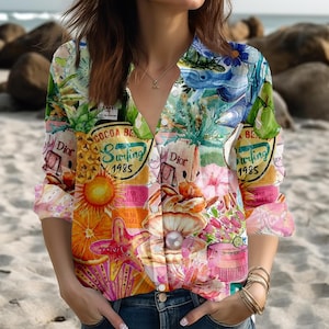 Könnte beinhalten: Ein farbenfrohes Hemd mit tropischem Thema. Das Hemd zeigt eine Collage von Bildern, darunter Ananas, Seesterne und den Text "Cocoa Beach Surfing 1985". Das Hemd hat einen V-Ausschnitt und lange Ärmel.