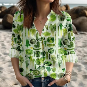 May include: A long-sleeved shirt with a light green backdrop, patterned with green vegetables such as lettuce, cucumbers, asparagus, and squash. The shirt features a V-neck and buttoned cuffs. The shirt is made of a light fabric.