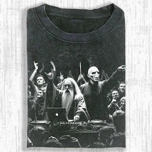 May include: Dark gray t-shirt featuring a black and white graphic of a wizard DJing at a concert with a crowd. The wizard is wearing a long white beard and robe. Other figures in the crowd are raising their hands in the air.