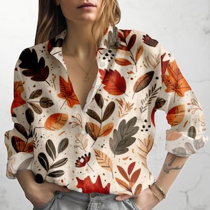 Könnte beinhalten: Langärmliges Hemd mit Knöpfen und einem Muster aus roten, orangefarbenen und braunen Herbstblättern auf beigem Hintergrund. Das Hemd hat einen Kragen.