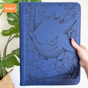 Puede incluir: Una carpeta para tarjetas rectangular de color azul con una ilustraci&oacute;n de l&iacute;neas azul oscuro del personaje Gengar rodeado de humo y estrellas. La esquina inferior derecha de la cubierta incluye el texto LIAM'S CARD VAULT en una fuente sans-serif.