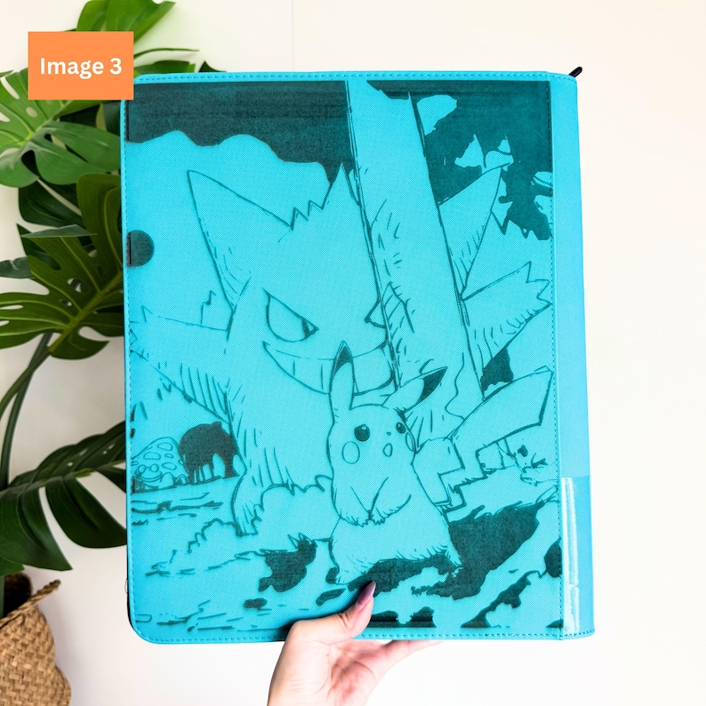 Puede incluir: Una carpeta rectangular de color turquesa con un estampado gr&aacute;fico en azul verdoso oscuro de los personajes Gengar y Pikachu. El dise&ntilde;o incluye una gran silueta de Gengar en el fondo y una figura detallada de Pikachu en primer plano.
